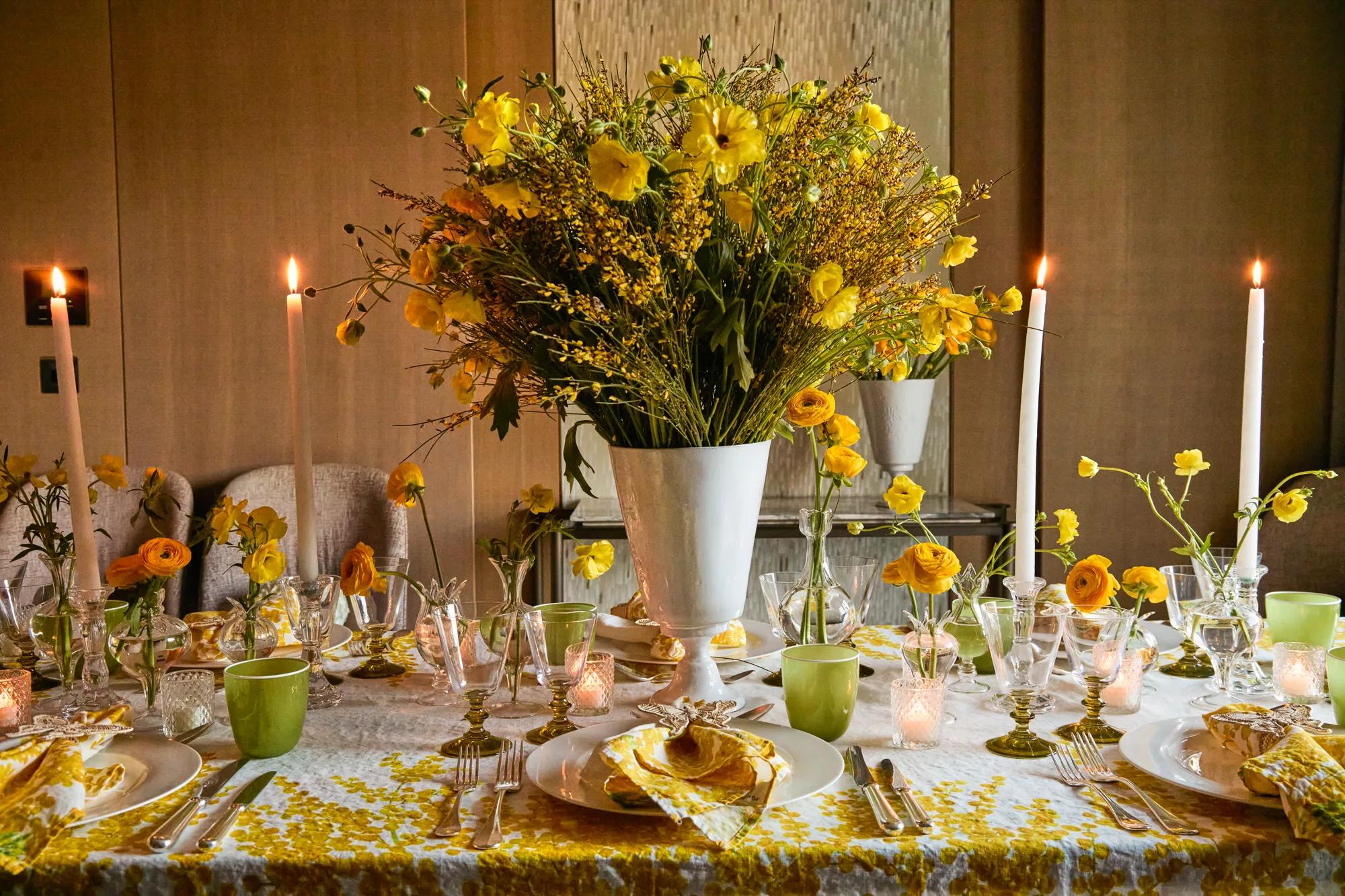 Elegant table setting with yellow floral arrangements, candles, and coordinated yellow and gold place settings.
