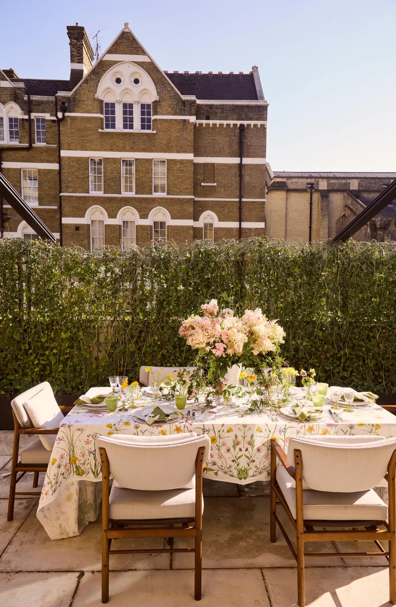Outdoor table set with floral centerpiece on a sunny terrace, overlooking a historic brick building.