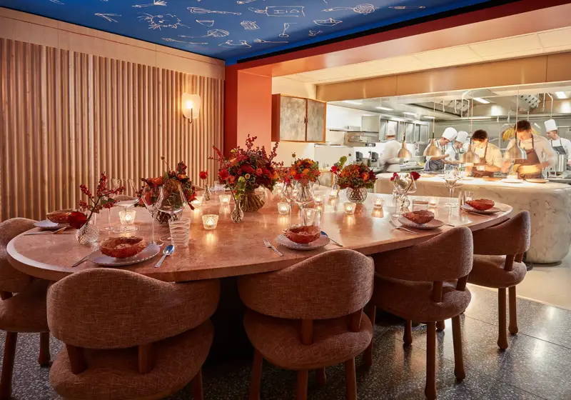 Private dining table set with flowers and candles beside an open kitchen with chefs preparing dishes.