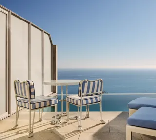 Private terrace with striped chairs, small round table, and sun loungers overlooking the calm blue sea.