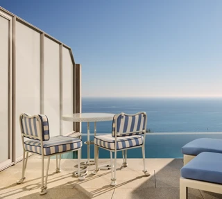 Private terrace with striped chairs, small round table, and sun loungers overlooking the calm blue sea.