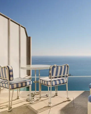 Private terrace with striped chairs, small round table, and sun loungers overlooking the calm blue sea.