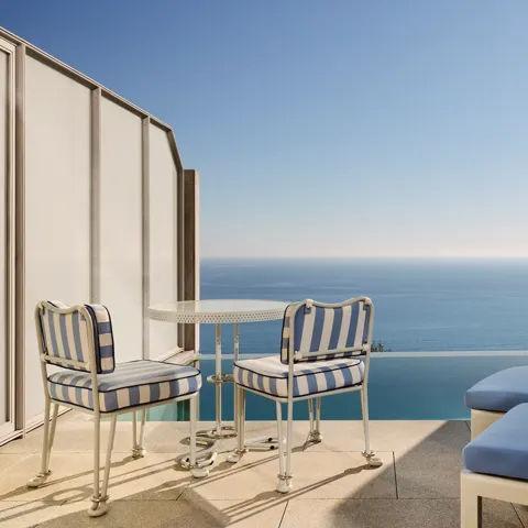 Private terrace with striped chairs, small round table, and sun loungers overlooking the calm blue sea.