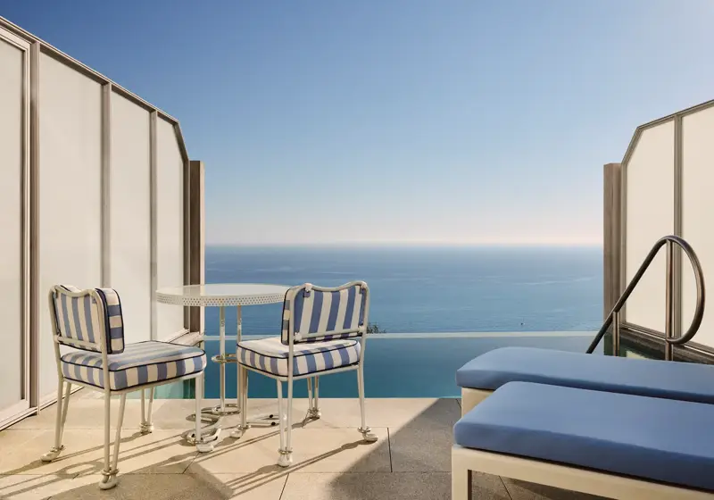 Private terrace with striped chairs, small round table, and sun loungers overlooking the calm blue sea.