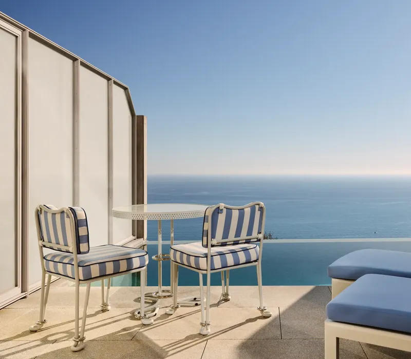 Private terrace with striped chairs, small round table, and sun loungers overlooking the calm blue sea.