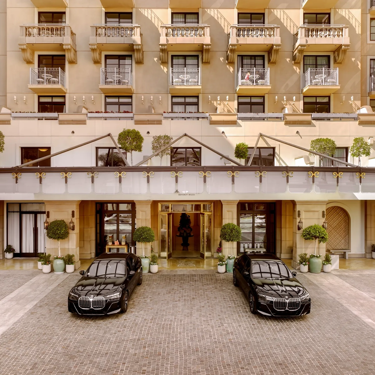 Porte-cochère at The Maybourne Beverly Hills with two black BMW sedan cars at the entry.