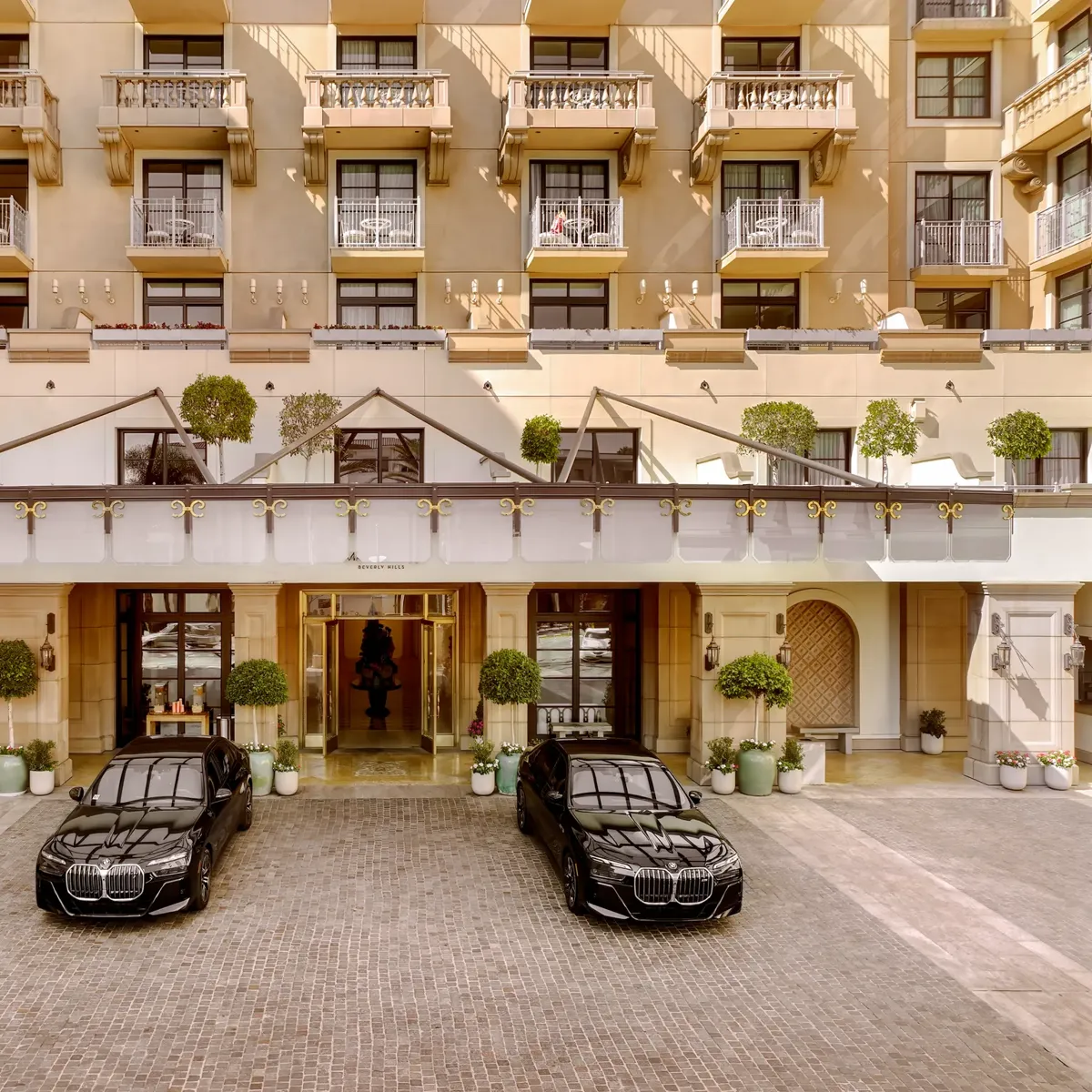 Porte-cochère at The Maybourne Beverly Hills with two black BMW sedan cars at the entry.
