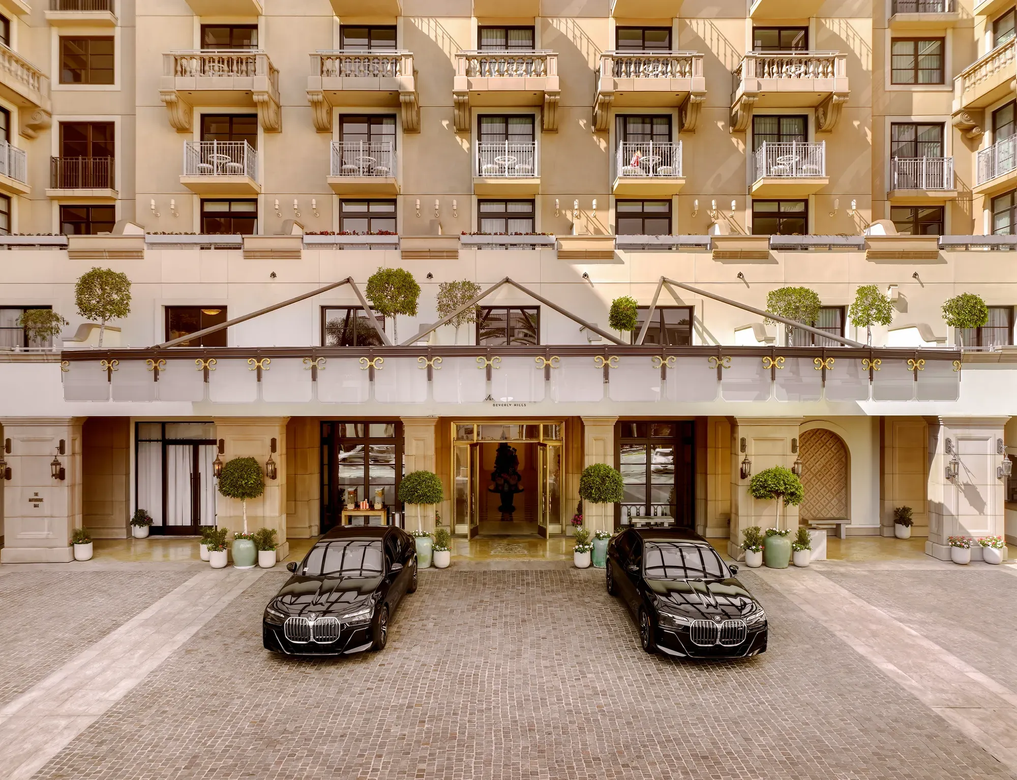 Porte-cochère at The Maybourne Beverly Hills with two black BMW sedan cars at the entry.