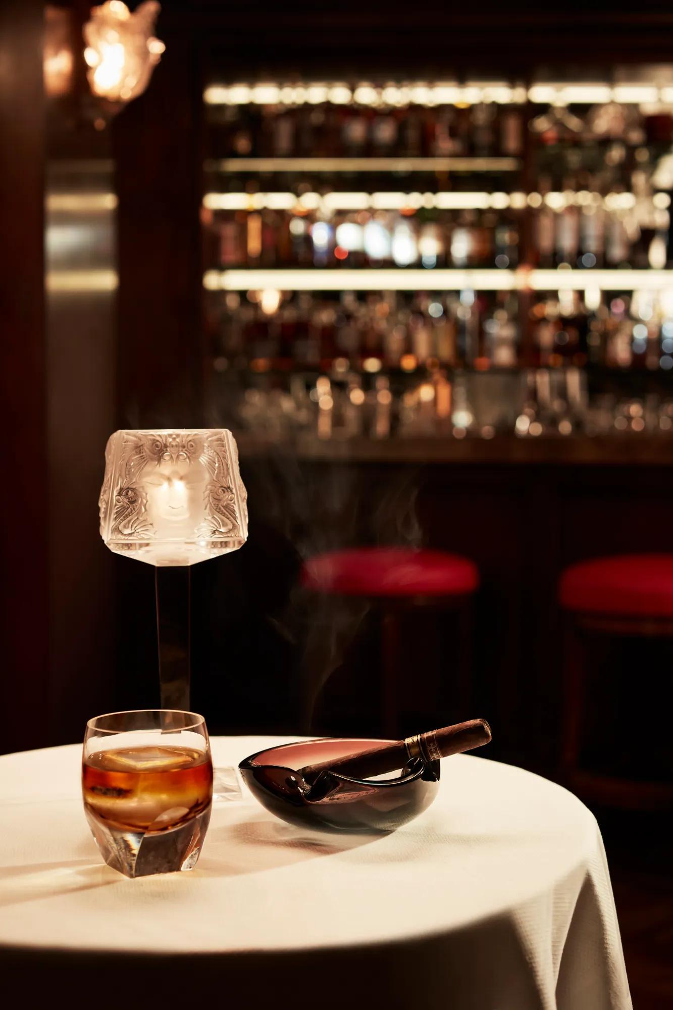 Whisky glass and smoking cigar on a round table in elegant bar setting.