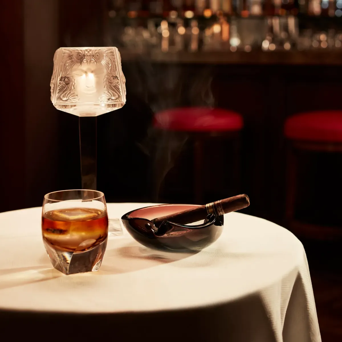 Whisky glass and smoking cigar on a round table in elegant bar setting.