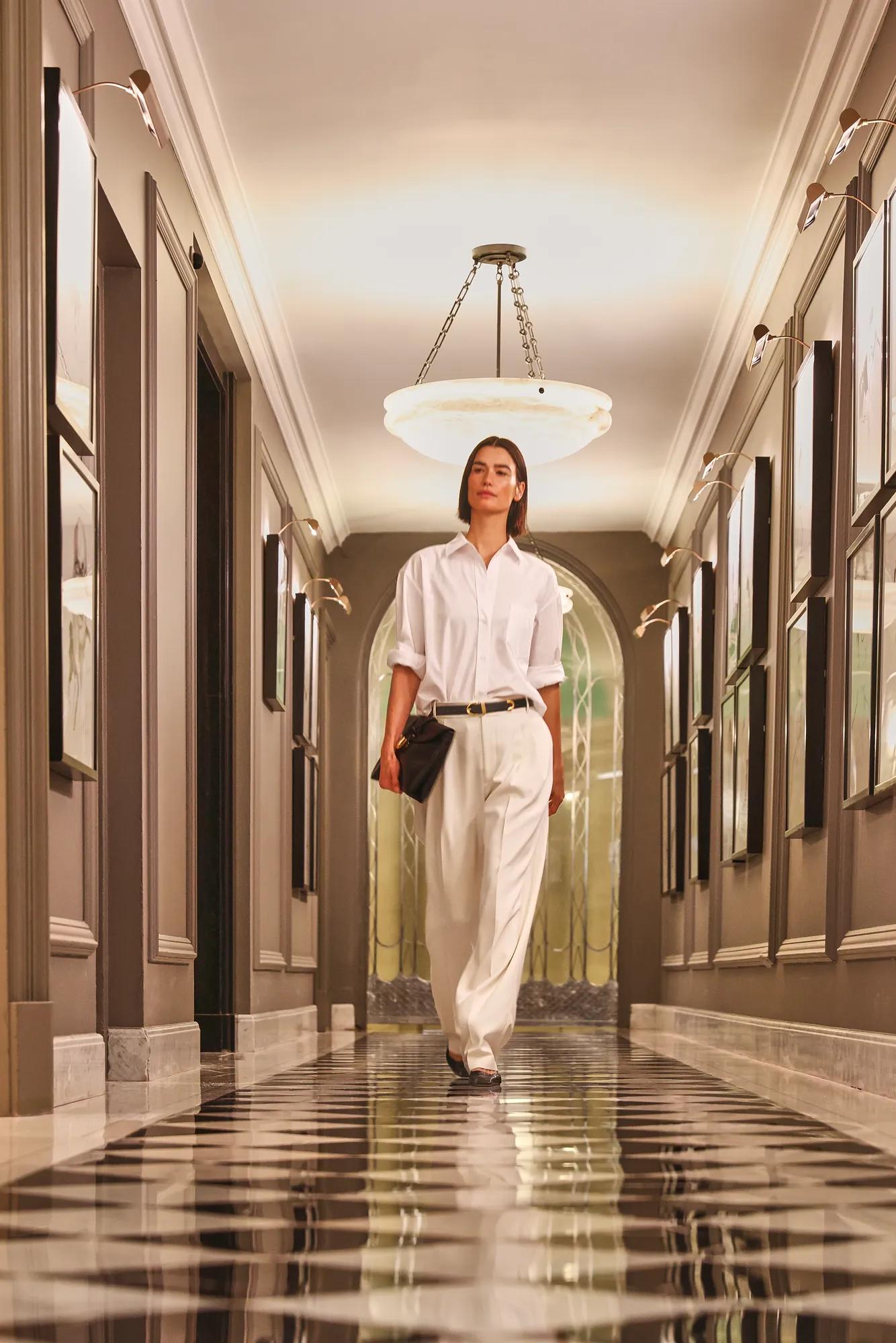 Guest walking through an elegant hotel corridor with a black-and-white tiled floor and statement chandelier.