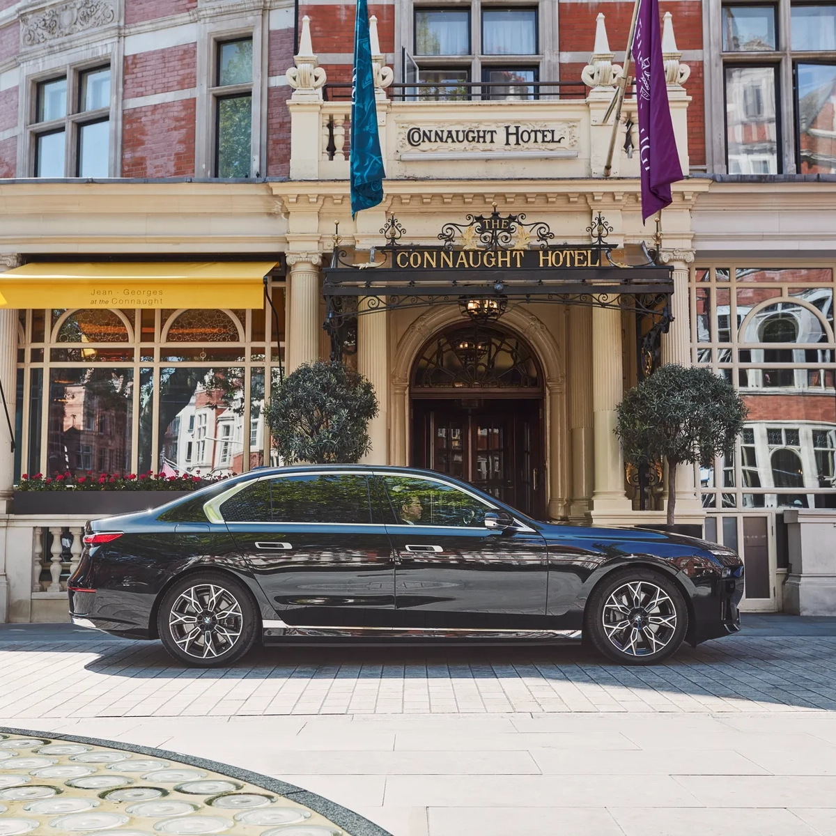 Black luxury car parked outside the hotel’s ornate entrance, with yellow awnings, arched windows and flags adorning the red-brick façade.