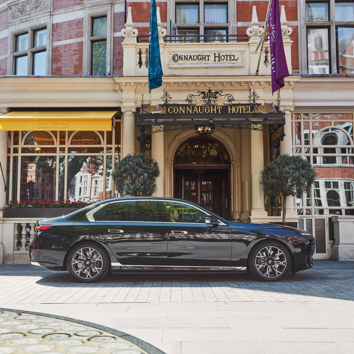 Black luxury car parked outside the hotel’s ornate entrance, with yellow awnings, arched windows and flags adorning the red-brick façade.
