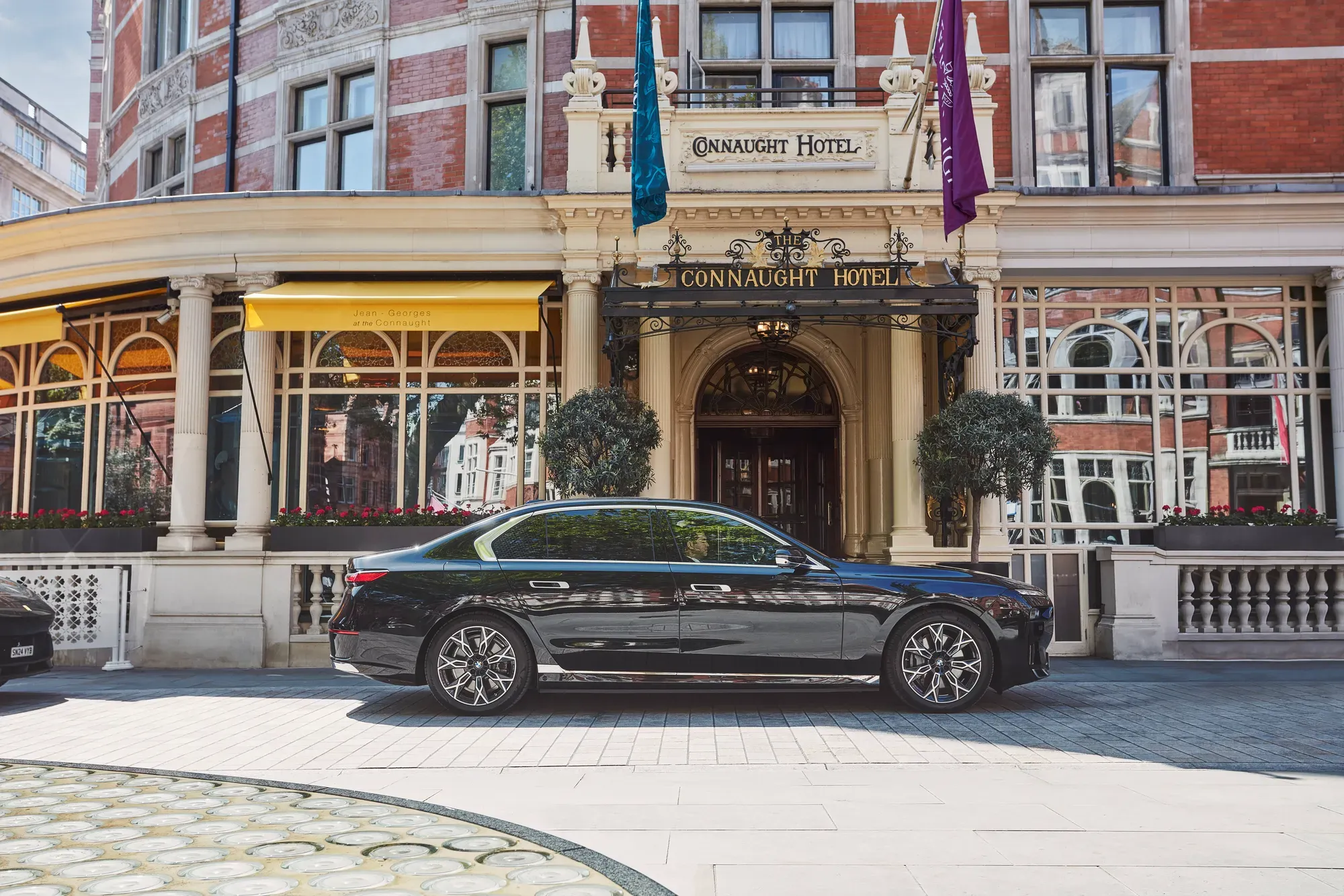 Black luxury car parked outside the hotel’s ornate entrance, with yellow awnings, arched windows and flags adorning the red-brick façade.