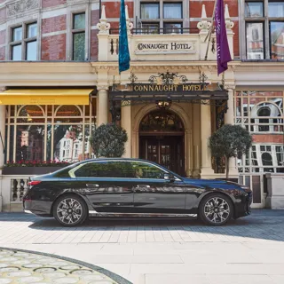Black luxury car parked outside the hotel’s ornate entrance, with yellow awnings, arched windows and flags adorning the red-brick façade.