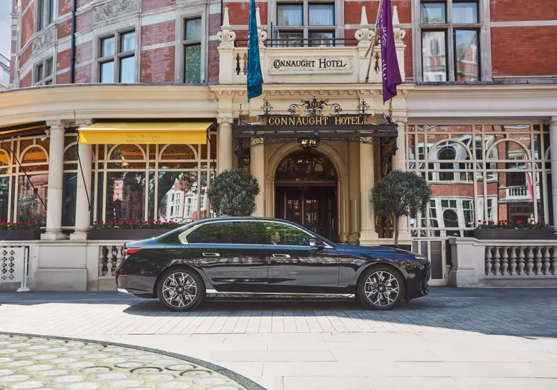 Black luxury car parked outside the hotel’s ornate entrance, with yellow awnings, arched windows and flags adorning the red-brick façade.