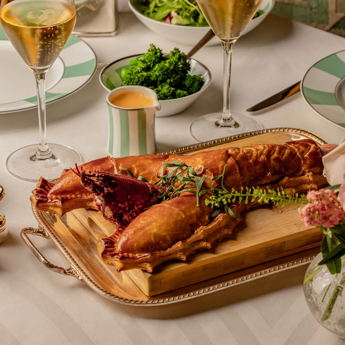 Lobster dish served on a wooden board with champagne, salad, and sides arranged on a neatly set dining table.