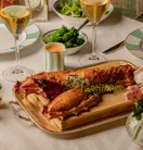 Lobster dish served on a wooden board with champagne, salad, and sides arranged on a neatly set dining table.