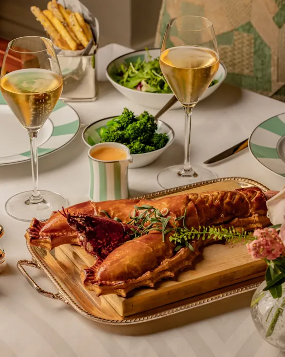 Lobster dish served on a wooden board with champagne, salad, and sides arranged on a neatly set dining table.