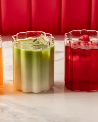 Three colourful iced drinks—citrus, green matcha, and raspberry—on a marble table against a red banquette.