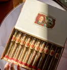 Open cigar box with neatly arranged cigars, a hand reaching toward them on a round table