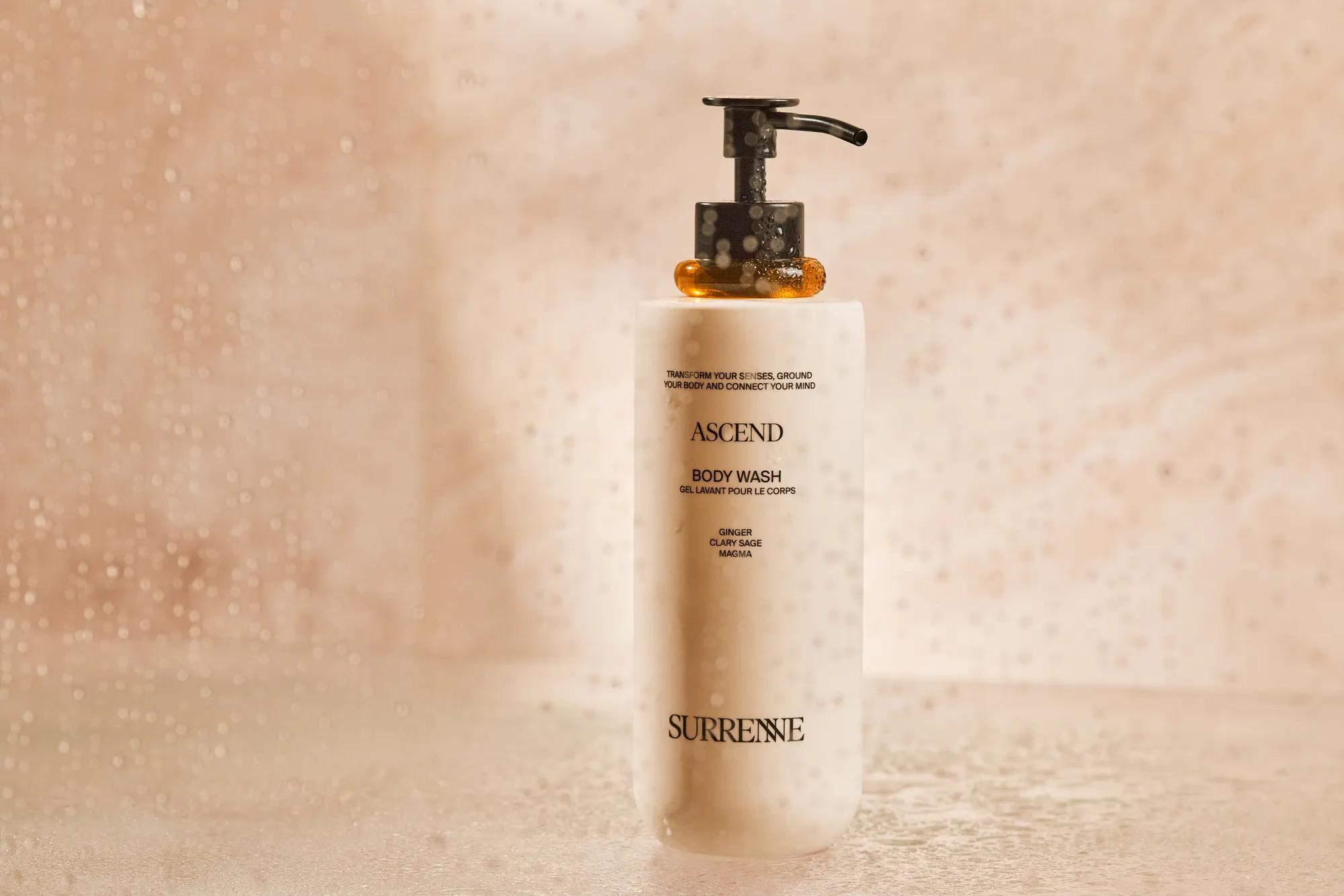 Surrenne Ascend body wash on a marble shower shelf with warm ambient lighting.