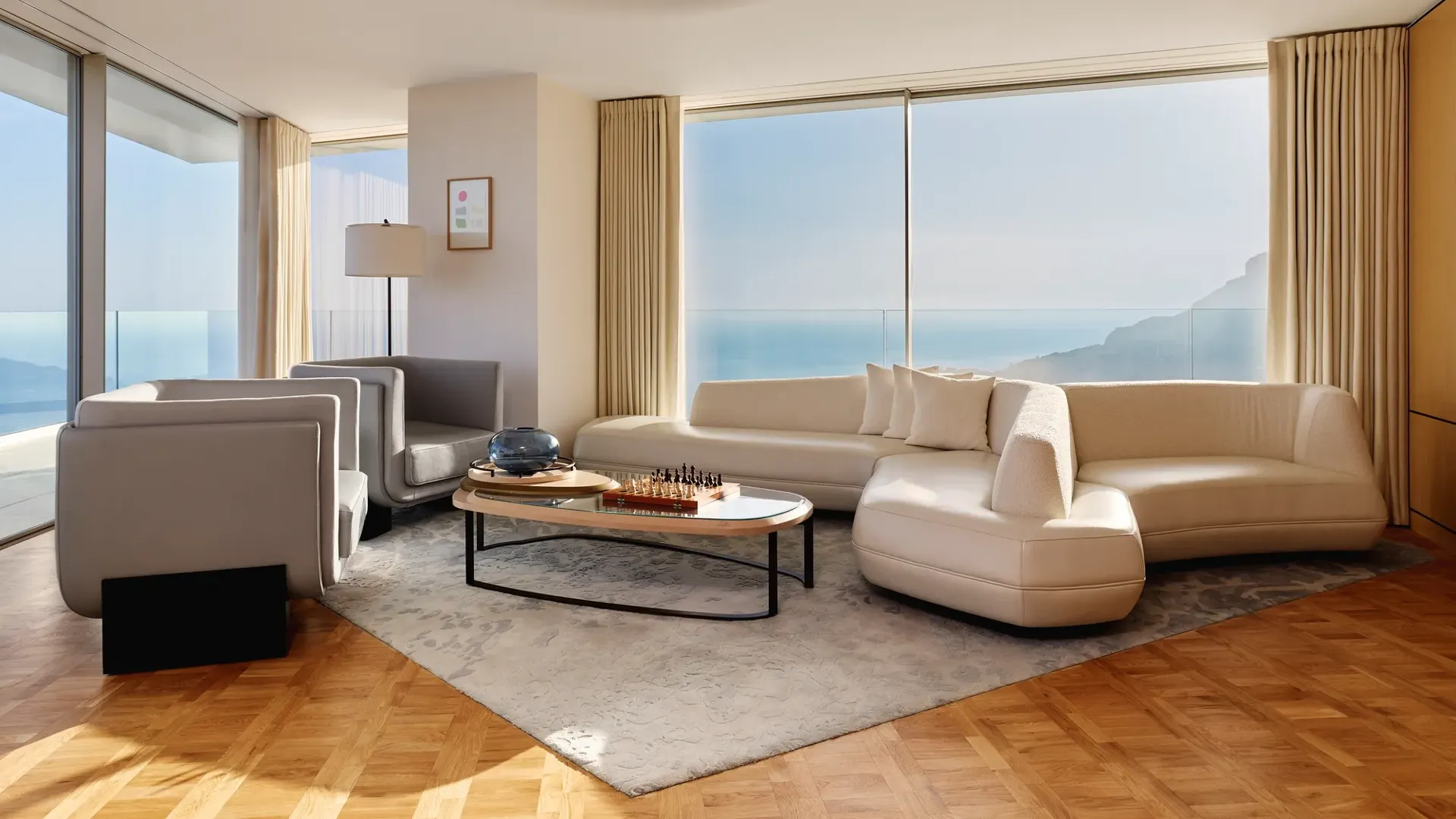 Salon moderne avec canapé blanc incurvé, fauteuils gris et table basse, doté de baies vitrées offrant une vaste vue sur la mer.
