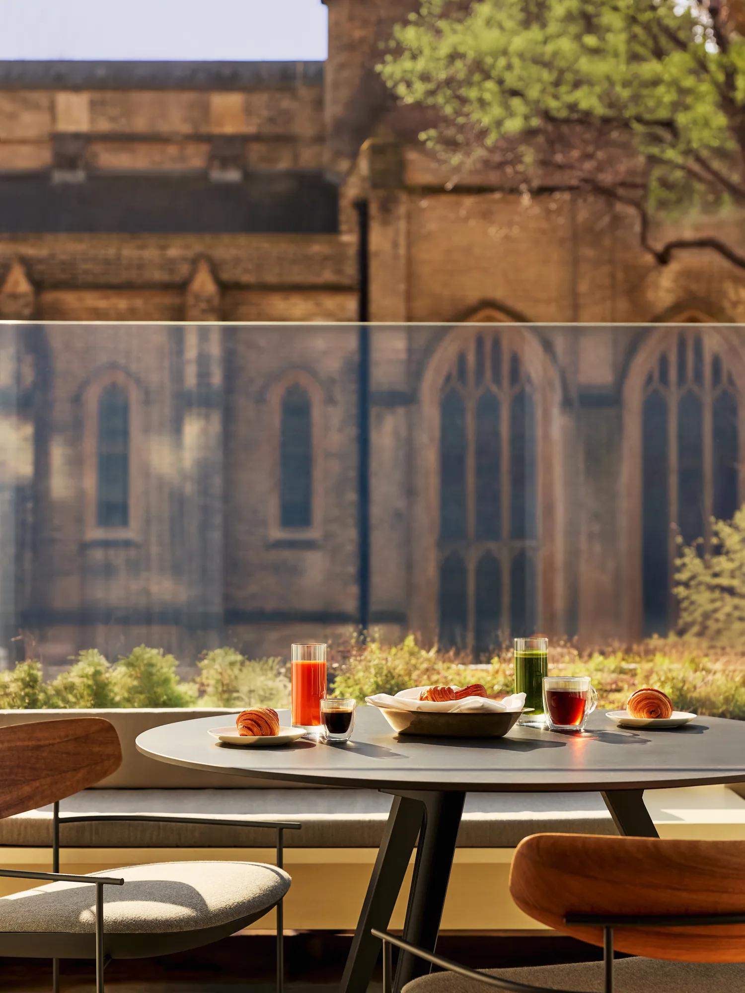 Terrace dining table with breakfast, chairs, and view of gothic church and green trees.