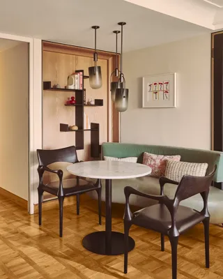 Dining nook with marble table, two chairs, built-in bench seating, shelving, and pendant lights.