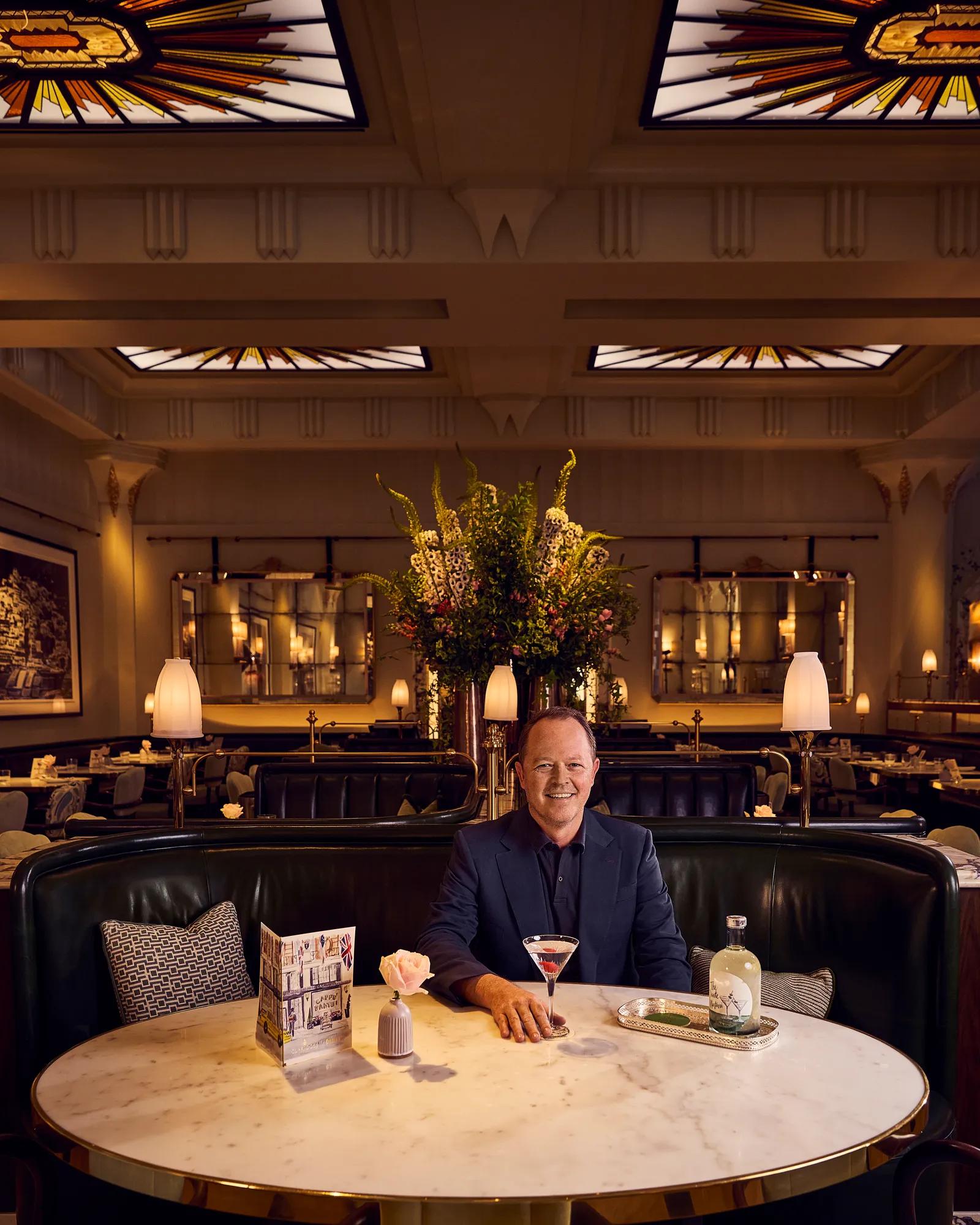 Person seated at a table in an elegant restaurant with a cocktail glass in front of them.