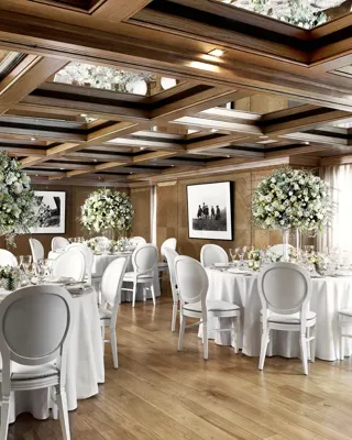 Elegant wedding dining room with round tables, white chairs, and tall floral centrepieces under a mirrored wooden ceiling.