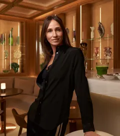 Woman standing at a marble bar in wellness lounge with decorative glassware in background.