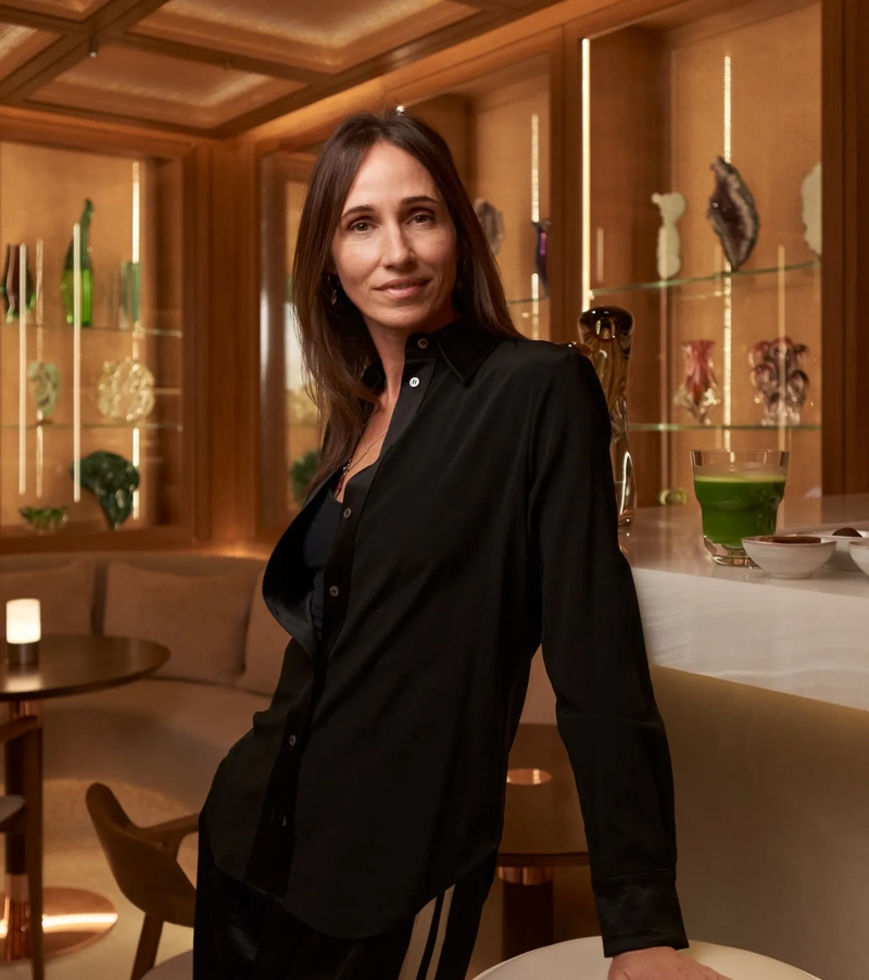 Woman standing at a marble bar in wellness lounge with decorative glassware in background.