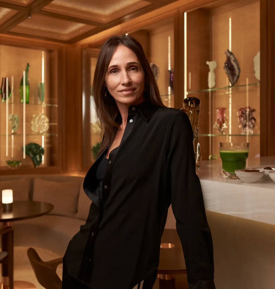 Woman standing at a marble bar in wellness lounge with decorative glassware in background.