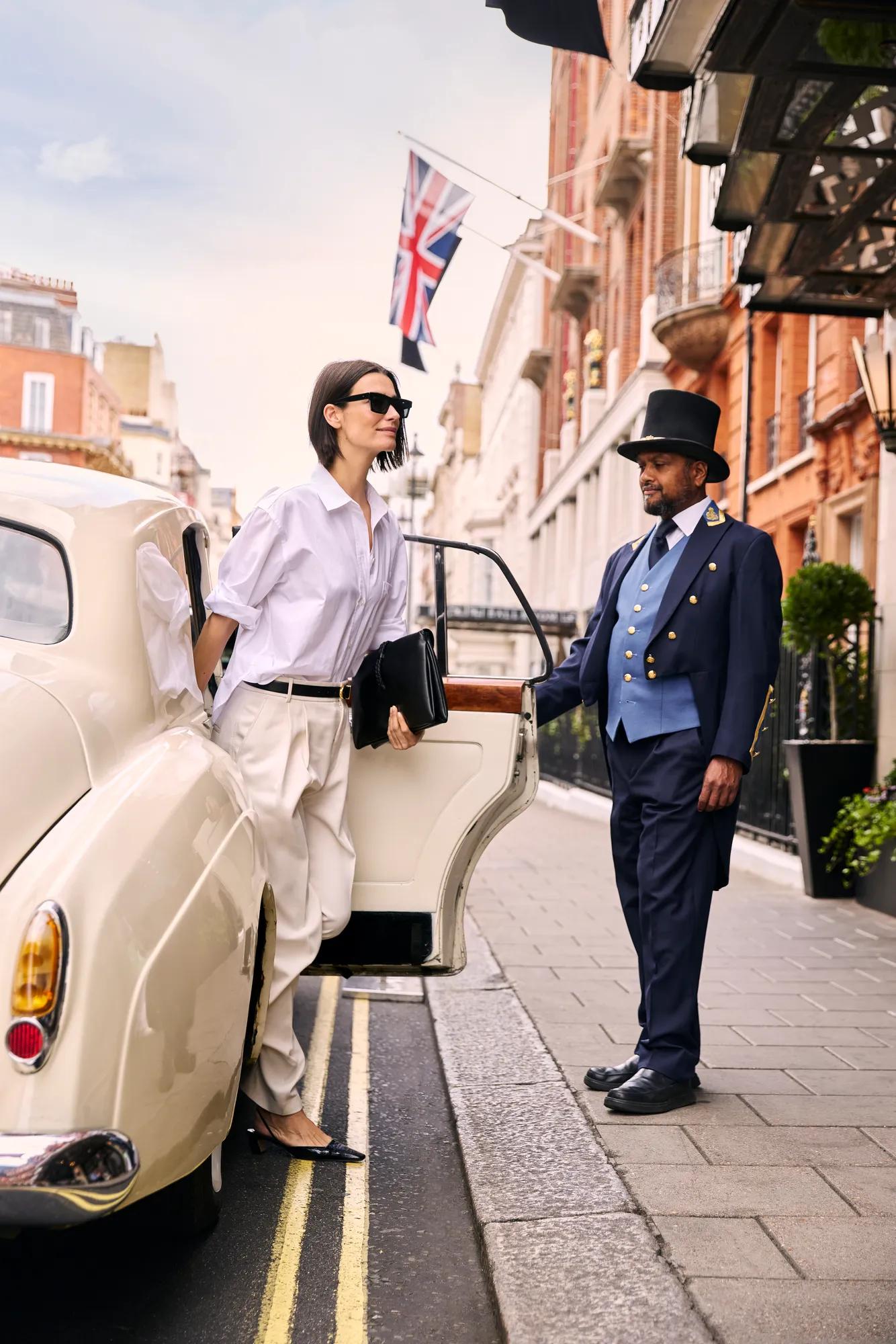 Guest stepping from a classic car outside a luxury hotel, welcomed by a doorman on a city street.