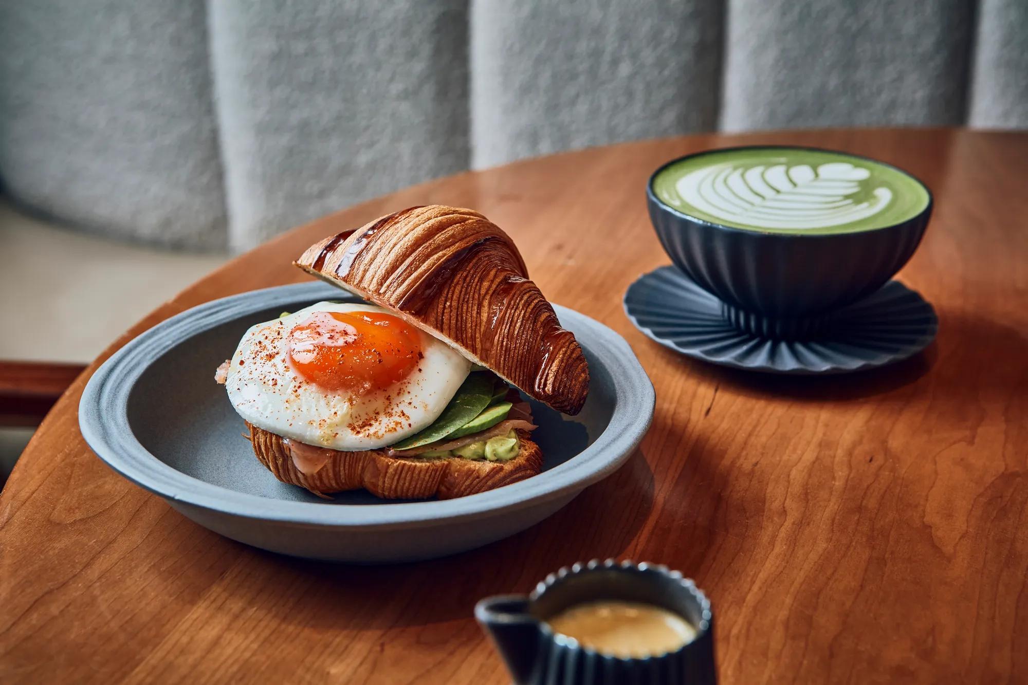 Salty breakfast croissant as well as matcha on a wooden table