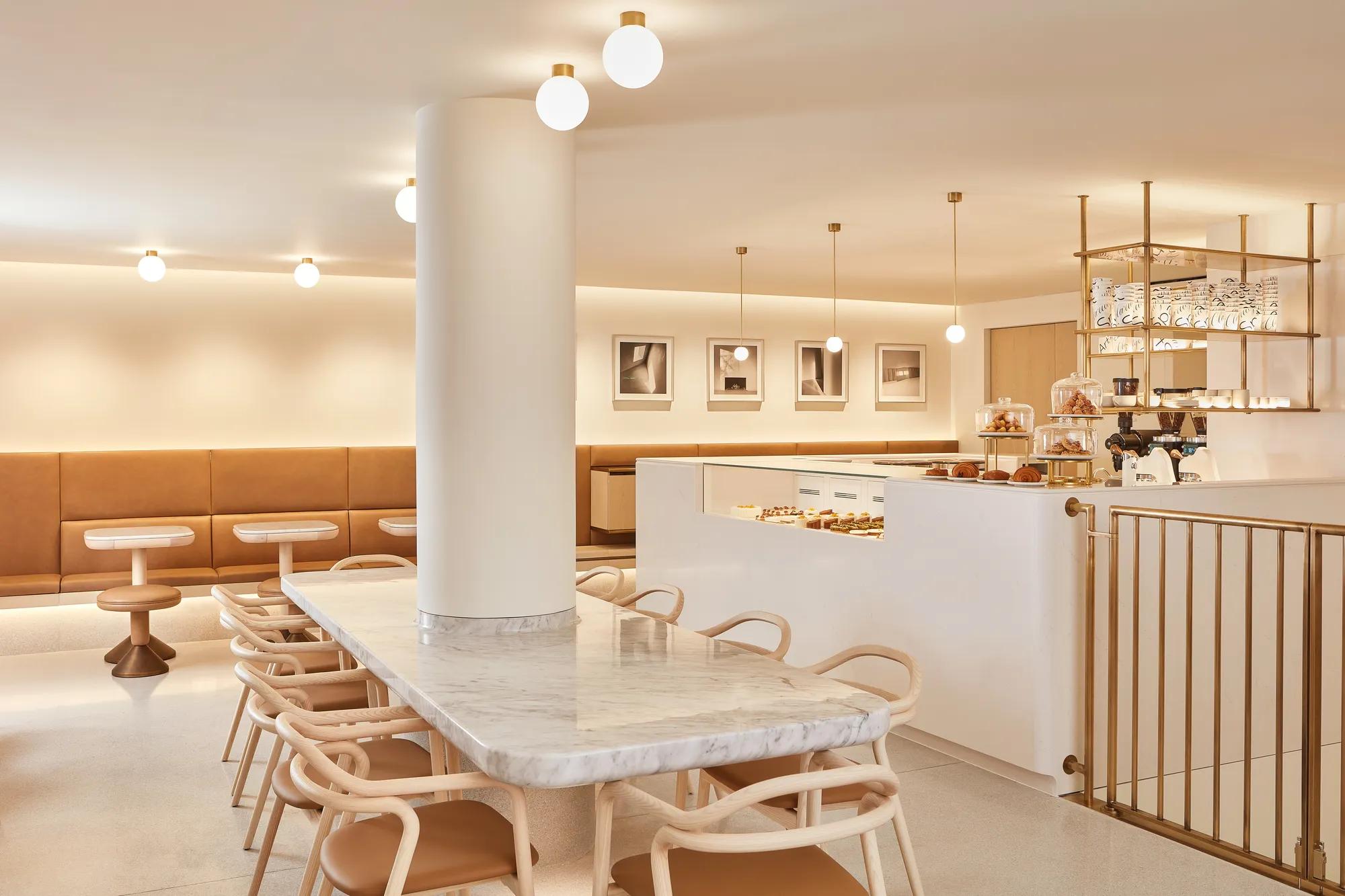 Modern café with marble table, tan seating, pastry counter and warm pendant lighting.