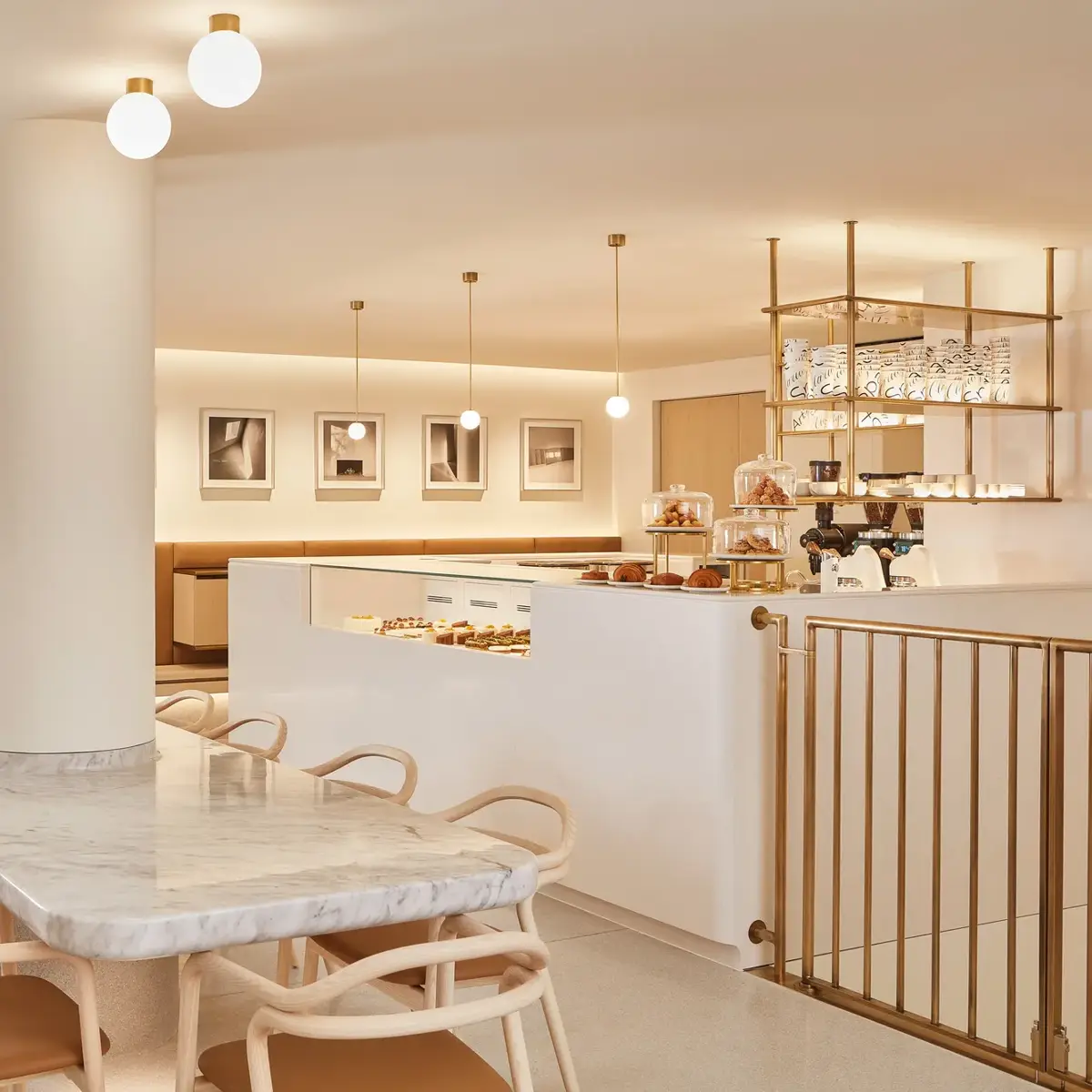 Modern café with marble table, tan seating, pastry counter and warm pendant lighting.
