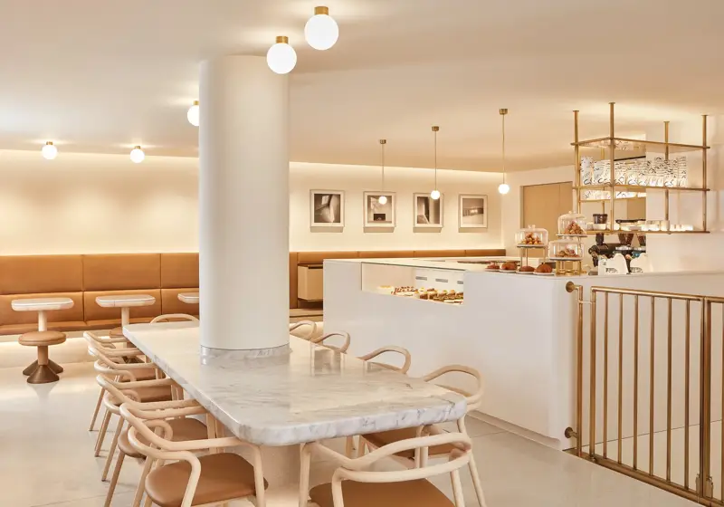 Modern café with marble table, tan seating, pastry counter and warm pendant lighting.