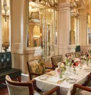 Elegant private dining room at Claridge’s featuring a long table set with white linens, floral centrepieces, and vintage-style chairs beneath mirrored Art Deco arches.