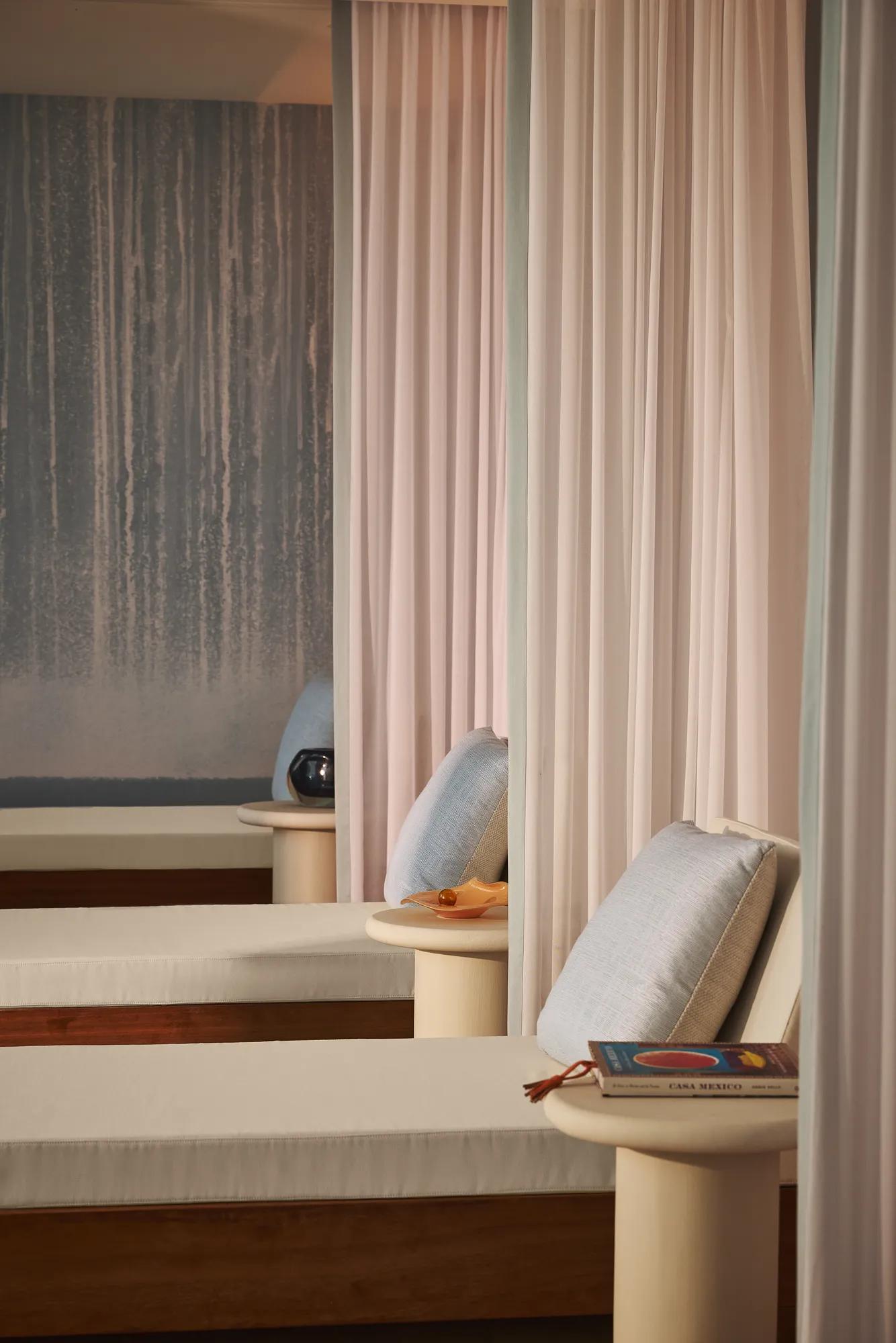 Salon de détente avec lits de repos coussinés, voilages légers et petites tables, créant une atmosphère apaisante de spa