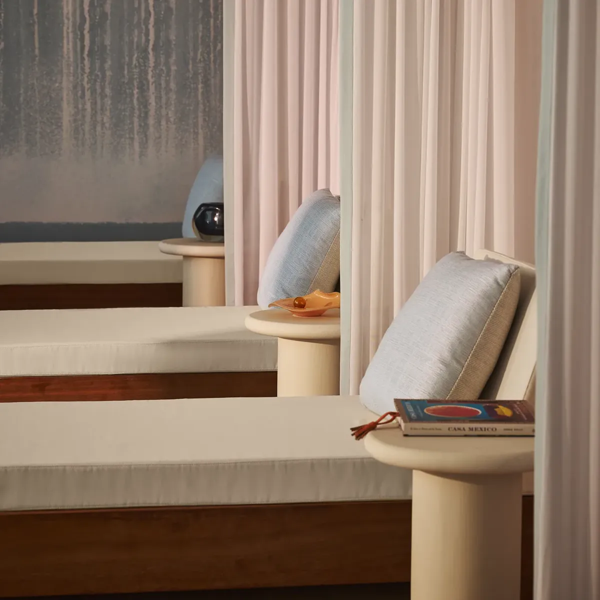 Salon de détente avec lits de repos coussinés, voilages légers et petites tables, créant une atmosphère apaisante de spa