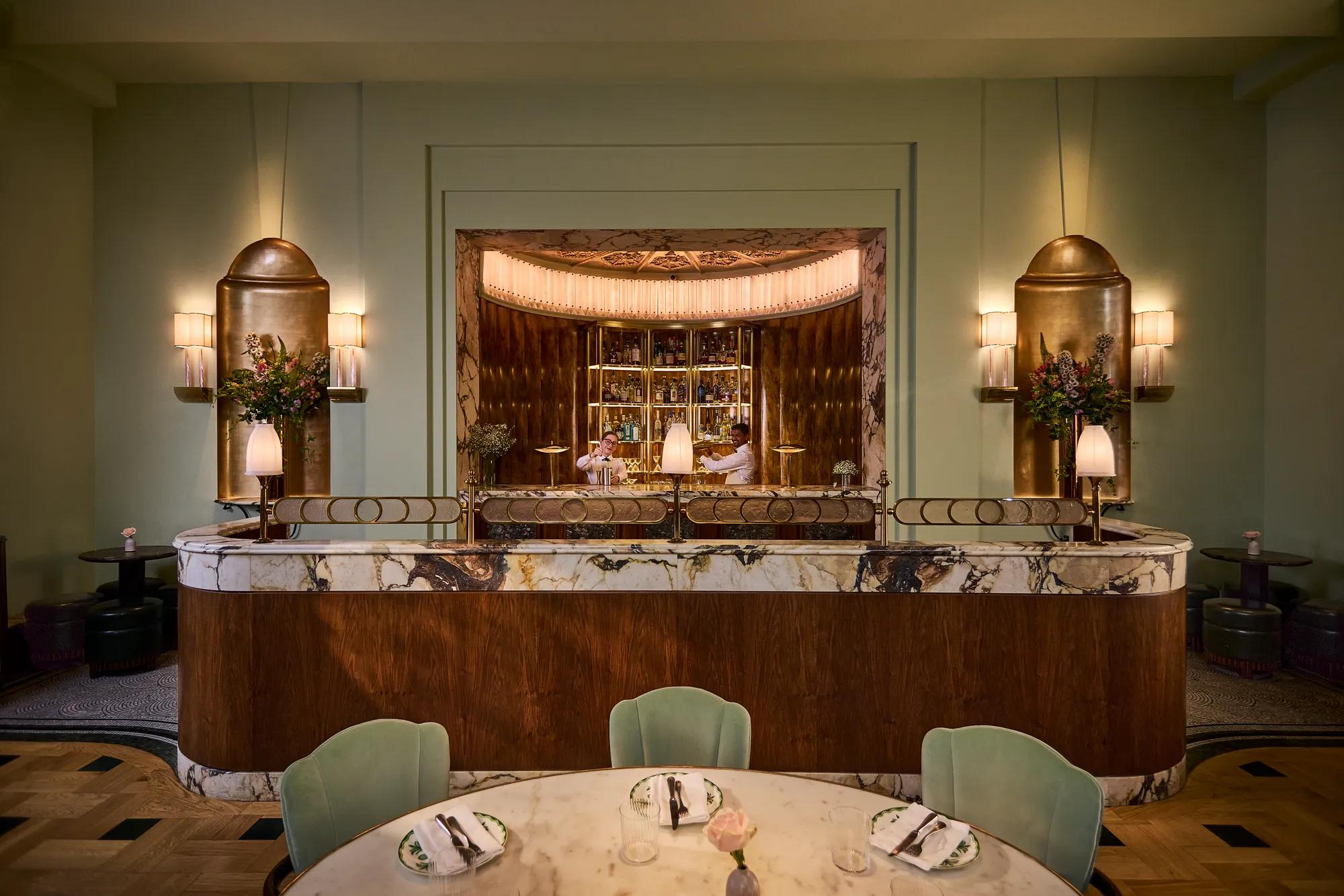 Elegant bar area with marble finishes, soft lighting, and tables set for dining.