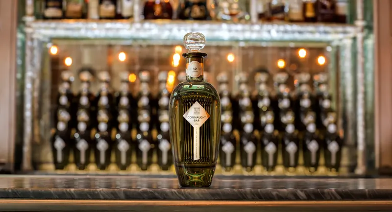 Connaught Bar bottle displayed on marble counter before illuminated back bar shelves.