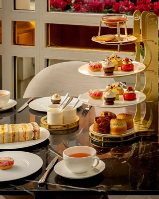 Afternoon tea table with tiered pastries, finger sandwiches, scones, and cups of tea on a marble surface.