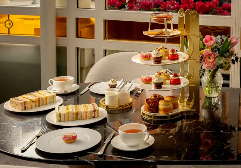 Afternoon tea table with tiered pastries, finger sandwiches, scones, and cups of tea on a marble surface.