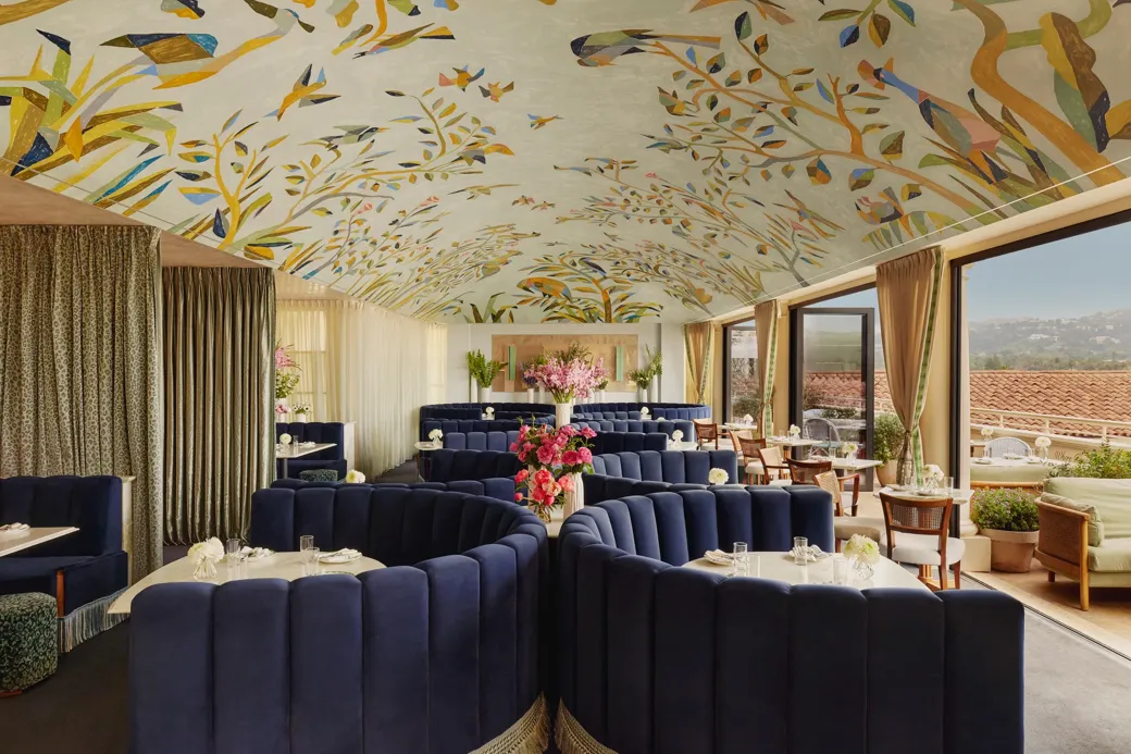Wide view of Dante Beverly Hills dining room—mural ceiling, curved navy booths, and doors opening to a sunlit terrace.