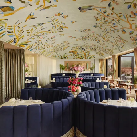 Wide view of Dante Beverly Hills dining room—mural ceiling, curved navy booths, and doors opening to a sunlit terrace.