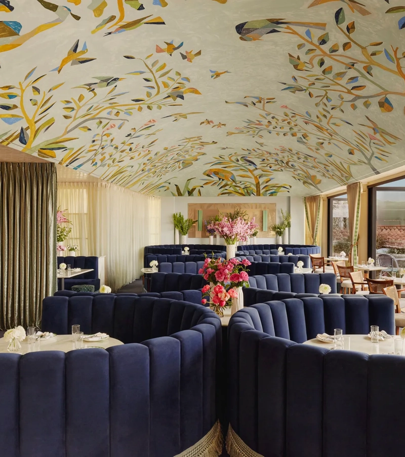 Wide view of Dante Beverly Hills dining room—mural ceiling, curved navy booths, and doors opening to a sunlit terrace.