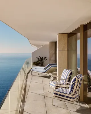Spacious balcony with striped chairs, sun loungers, and glass railing, offering panoramic sea views beneath a clear sky.
